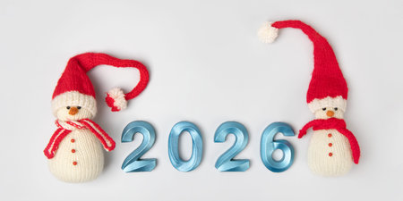 Knitted toy snowman in red hat and scarf with blue numbers 2026 on gray background. New Years...