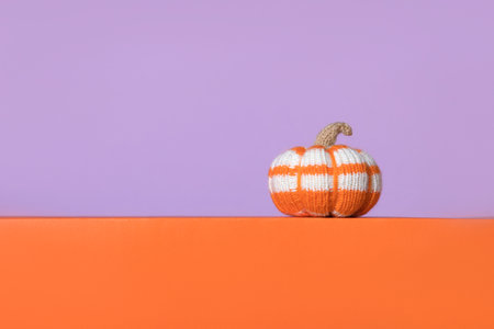Knitted white and orange pumpkin on purple background, front view. Halloween concept. Handmade knitted toys for children and holiday home decor.の写真素材