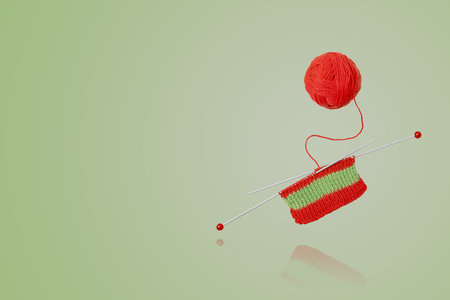 Red and green knitted wool on green background with knitting needles for knitting warm clothes and hobbies needlework. Knitting a striped scarf with red and green threadsの写真素材