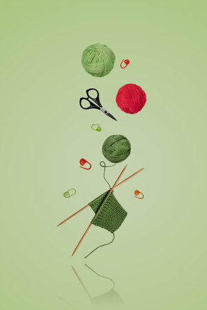Tools for knitting warm clothes: scissors, green and red ball of thread, stoppers, and knitting needles with a knitted green piece of fabric flying in the air on a gray background. Hobby home crafts.の写真素材