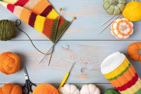 Cozy composition for needlework from basket with balls for knitting warm clothes, striped fabric for future scarf and knitted pumpkin toys on table with knitting needles, crochet hooks and scissors.の写真素材