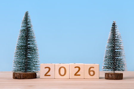 New Year 2026 postcard. Wooden cubes with numbers and green Christmas trees on a wooden table and a blue background.の写真素材