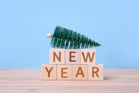 Wooden cubes with the word New Year and green Christmas tree on a wooden table and a blue background. Christmas and New Year design holiday cardの写真素材
