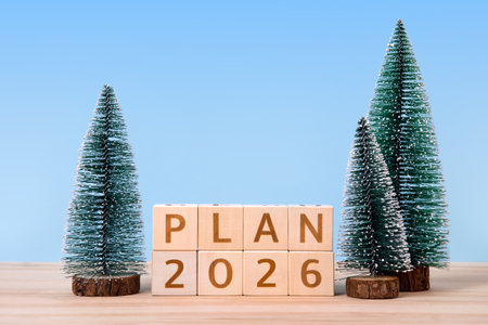 New Year 2026 and Christmas postcard. Wooden cubes with numbers 2026 and word plan and green Christmas trees on a wooden table and a blue background.の写真素材