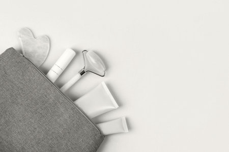 Demonstrating the colors of 2026 - Cloud Dancer. Set of cosmetics for face care of tube of cream, gel and massagers jade roller, guasha in cosmetic bag on pink background.の写真素材