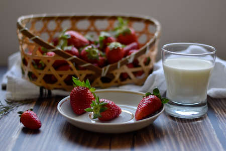 Strawberries on a white plate with gold rim and in wickered basket with a clear glass of milk. Wood background and white tea towel.の写真素材