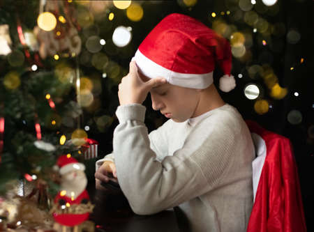 The kid wearing Santa hat is sitting with his tephoneの写真素材