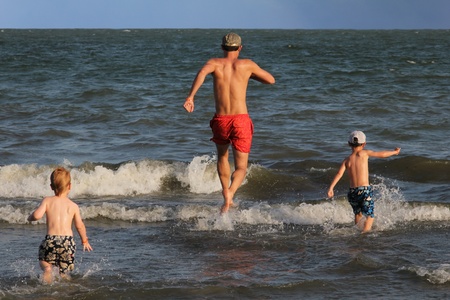 Father and his two sons running into the ocean and having funの写真素材