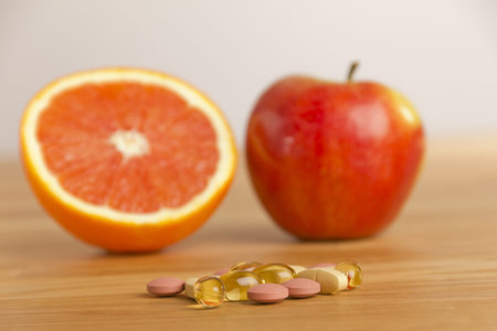 Dietary supplement lying ona table, behind an apple and and orange