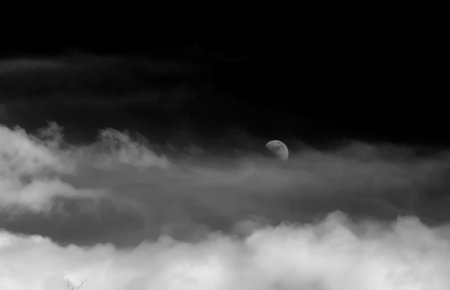 A black and white photo of the waxing moon floating in the clouds.の写真素材