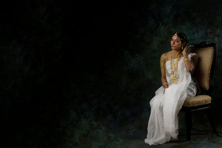 solo image of indian woman in a white saree wearing gold jewelry gold necklace gold bangles in a green solid backgroundの写真素材