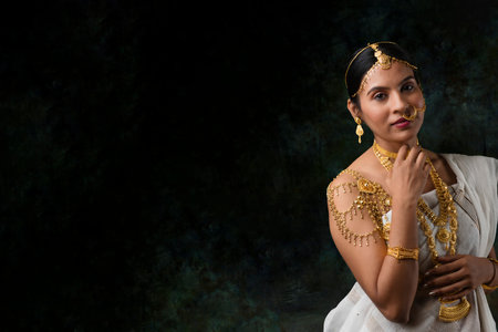 solo image of indian woman in a white saree wearing gold jewelry gold necklace gold bangles in a green solid backgroundの写真素材
