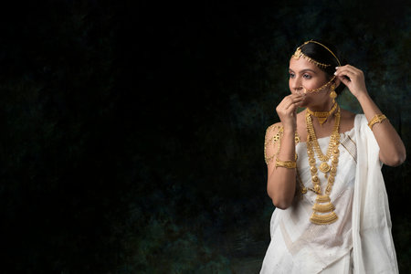 solo image of indian woman in a white saree wearing gold jewelry gold necklace gold bangles in a green solid backgroundの写真素材
