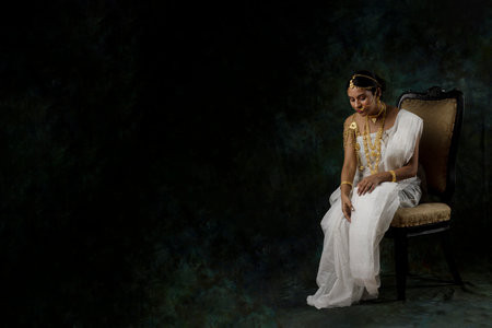 solo image of indian woman in a white saree wearing gold jewelry in a green solid backgroundの写真素材