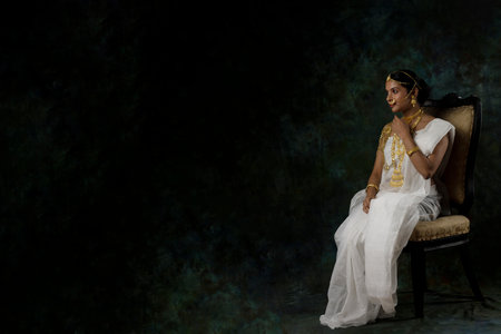 solo image of indian woman in a white saree wearing gold jewelry gold necklace gold bangles in a green solid backgroundの写真素材