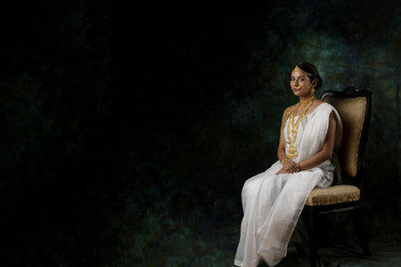 solo image of indian woman in a white saree wearing gold jewelry gold necklace gold bangles in a green solid backgroundの写真素材