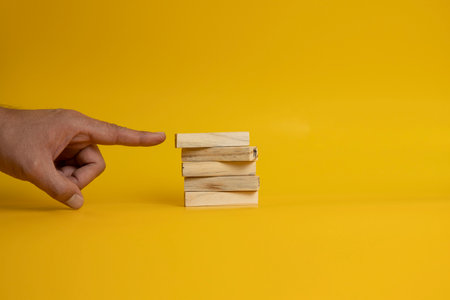An image featuring a hand pointing a finger at a stack of wooden blocks arranged neatly on a solid yellow background.の写真素材