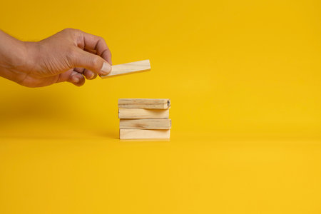 placing a wooden blocks on two more blocks arranged neatly on a solid yellow background.の写真素材