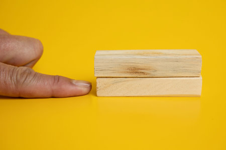 An image featuring a man pointing a finger at two blocks arranged neatly on a solid yellow...