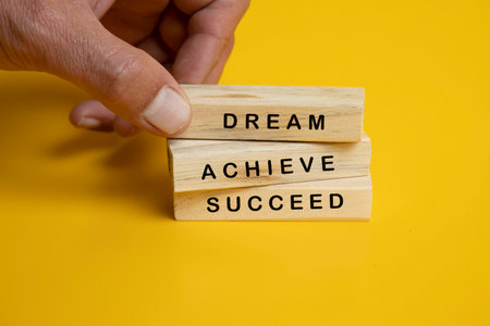 An image featuring three wooden Jenga blocks arranged neatly on a solid yellow background. Each block is engraved with an inspirational word or phraseの写真素材