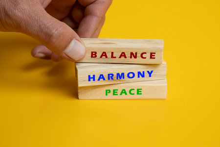An image featuring three wooden blocks arranged neatly on a solid yellow background. Each block is engraved with an inspirational word or phrase, such as "Believe," "Achieve," and "Dream." The bright yellow backdrop enhances the message of positivity and motivation, making it ideal for stock photography focused on personal growth, success, and encouragement. The clean, minimalist design emphasizes the power of words and their impact on one's mindset.の写真素材
