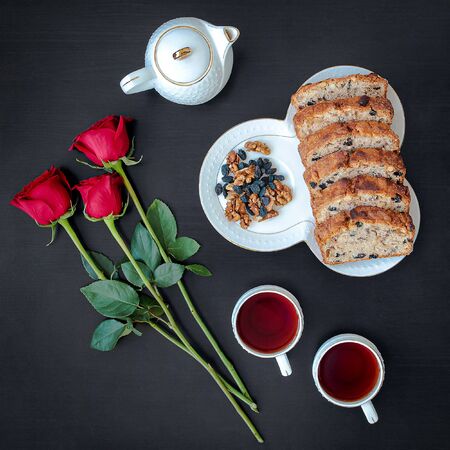 Delicious homemade Cake roll with tea-set, red roses on the black background, top viewの写真素材