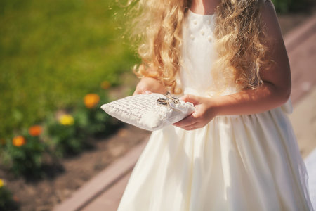 The little girl in a white dress carries a pillow on which lay the wedding ringの写真素材