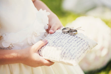 The little girl in a white dress carries a pillow on which lay the wedding ringの写真素材