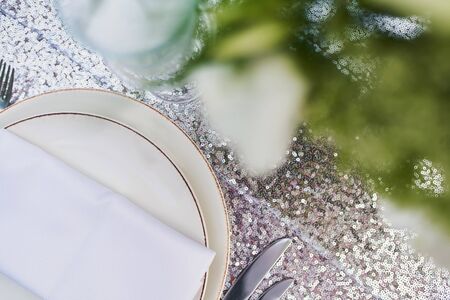 Plate, glass and cutlery with a white napkin on a beautiful tablecloth with patterns through the greens. Preparing summer birthday celebration outdoors. Knife, fork and dishes before the holidayの写真素材