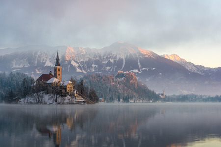 Lake Bled in the winter morning: the snowy island with mountains and castle in the backgroundのeditorial素材