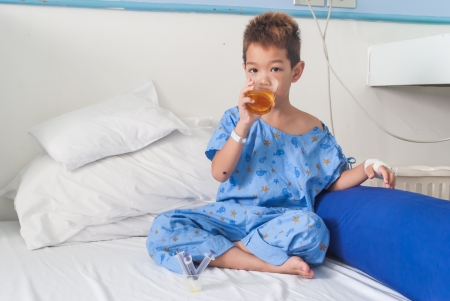 Asian patient boy with saline intravenous  iv  on hospital bed  Are using the tablet and eating medicines の写真素材