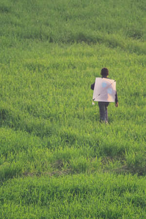 A boy running in the fields with a kite on his backの写真素材