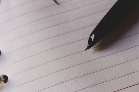 Closeup of a pen tip and an empty notebook on the tableの写真素材