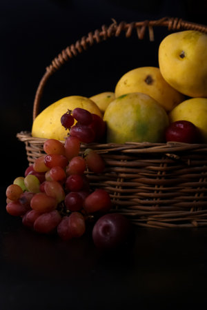 basket of full of fruits with summer seasonal fruits farm fresh mangoes and red wine grapesの写真素材