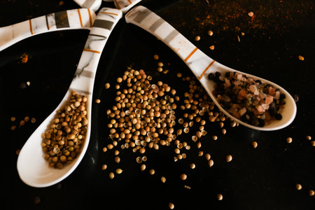spoon full of black pepper and coriander seeds on black background food photography closeupの写真素材