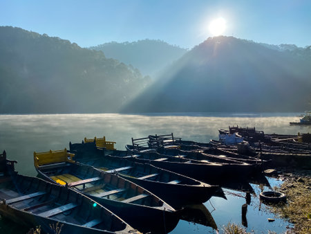 landscape view of foggy lake with sunlight showering over the mountains on it with row boats scenic viewの写真素材