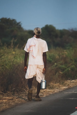 An old Indian man with a milk can walking on the road, India. Indian culture tradition roadsideの写真素材