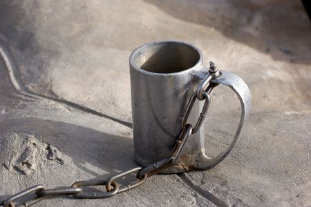  A metal mug for water with a chain near to a source.の写真素材