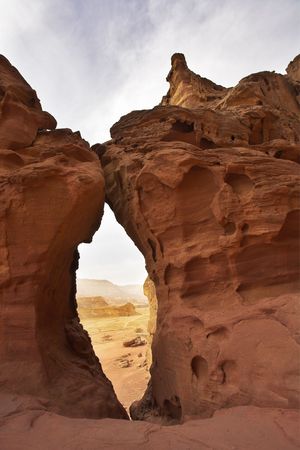 Through huge arch in ancient red mountains in desert of Israelの写真素材