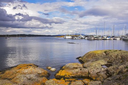 Picturesque coastal stones on coast of ocean passage, overgrown mosses, and sailing yachtsの写真素材