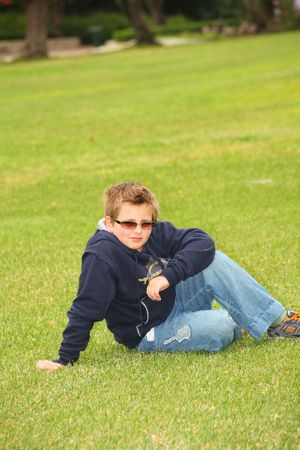 The beautiful boy in protective solar glasses has a rest on a green lawn in parkの写真素材