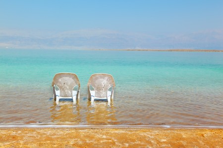 Two white beach chairs stand near the water at the beach. Dead Sea, Israelの写真素材