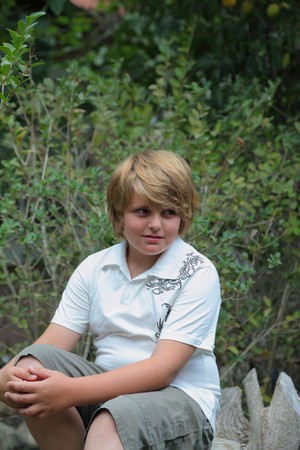 A beautiful blond boy poses for the photographer, sitting in the gardenの写真素材