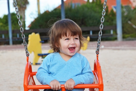 The beautiful little boy in blue sweater  laughs cheerfully at a red swingの写真素材
