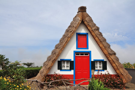 Pastoral landscape. Small rural house with a triangular thatched roof. The red door and small windows with shutters. Madeira, the city of Santanaのeditorial素材