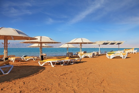A magnificent beach with clean yellow sand on the shore of the Dead Sea. Guests of the hotel - beach umbrellas and beach loungersの写真素材