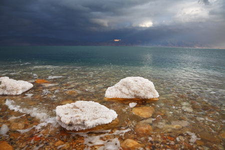 Winter on the Dead Sea  Blue storm cloud, green water and rocks, overgrown with salt