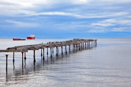 Abandoned pier. Old dilapidated pier in the Strait of Magellan. In the distance the two cargo shipsの写真素材
