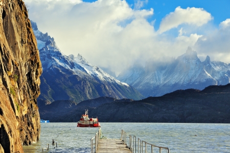 National Park Torres del Paine, Chile  Pier on Lake Grey  Red tourist ship sails to the dock  In the mountains around the lake are piled clouds  Summer sun illuminates the lake の写真素材