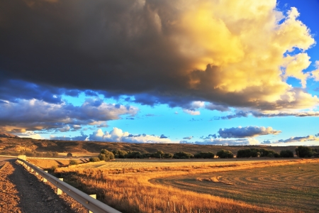 The enormous storm cloud and a flat plain covered in orange sunset.  In the steppe runs a gravel road. Storm over the Pampasの写真素材